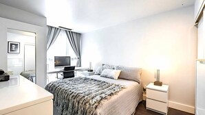 Una camera da letto moderna con un letto, comodini, una scrivania con un computer e una finestra con tende.