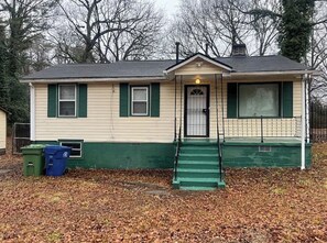 A single-story house with a front porch, a door with a small window, and a chimney. - 4BR Home Minutes from Mercedes‑Benz Stadium — FIFA 2026 Full‑Event Rental (Atlanta)