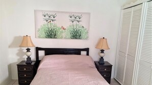 Une chambre à coucher avec un lit, deux tables de chevet, une lampe sur chacune, un tableau au-dessus du lit et une armoire sur le côté droit.