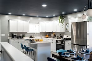 A modern kitchen with white cabinets, a central island, bar stools, and a stainless steel refrigerator. - Luxury Hocking Hills Cabin| Views + Epic Game Room (South Bloomingville)