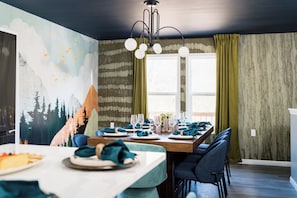 A dining area with a mural, a chandelier, and a table set for four. - Luxury Hocking Hills Cabin| Views + Epic Game Room (South Bloomingville)