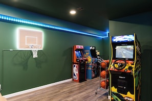An indoor arcade with basketball and racing game machines, a basketball hoop, and blue LED strip lighting. - Luxury Hocking Hills Cabin| Views + Epic Game Room (South Bloomingville)