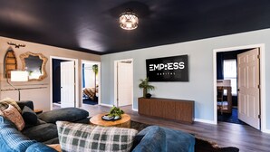 Ein modernes Wohnzimmer mit dunkler Decke, einem an der Wand befestigten Fernseher und einem Schild mit der Aufschrift 'EMPRESS CAPITAL'.