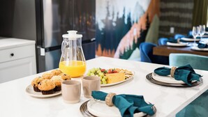 Ein Frühstückstisch mit einem Orangensaftkrug, Muffins und einer Fruchtschale.