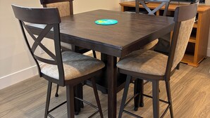 Un coin repas comprenant une table rectangulaire, quatre chaises, un téléviseur et une fenêtre avec des stores.