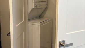 Une buanderie équipée d’un lave-linge et d’un sèche-linge superposés, d’une porte avec une poignée et d’un plancher en bois.