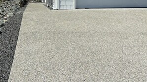 Un garage attenant à une maison, avec une allée en béton, une clôture en bois et un mur en pierre.