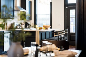 A modern kitchen with dark cabinetry, a central island, and a dining area with chairs. - Lou Luxe- Speakeasy, EPIC Arcade, Hottub & FirePit (St. Louis)