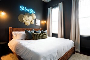 A neatly made bed with a headboard, a neon sign reading 'St. Louis Blues,' and a wall-mounted drum set. - Lou Luxe- Speakeasy, EPIC Arcade, Hottub & FirePit (St. Louis)