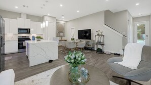 Eine moderne Küche mit Kochinsel, ein Essbereich mit Fernseher und ein Wohnzimmer mit Sofa und dekorativer Vase.