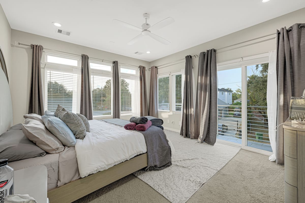 A bedroom with a bed, curtains, a ceiling fan, and a view through the window.