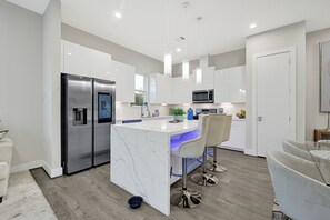 A modern kitchen with white cabinets, stainless steel appliances, and a marble island. - Empress Hope House (Houston)