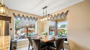 A dining area with a large table, chairs, a chandelier, and a view of a pool and garden. - Empress Villa Retreat (Alvin)