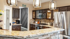 A modern kitchen with granite countertops, a built-in island, stainless steel appliances, and pendant lighting. - Empress Villa Retreat (Alvin)