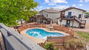 Un patio trasero con piscina, terraza de madera y una casa con puerta azul y balcón.