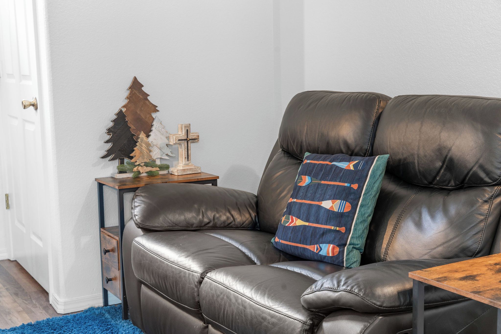 A leather sofa with a decorative pillow, a small wooden table with a cross and Christmas tree decoration, and a blue rug.