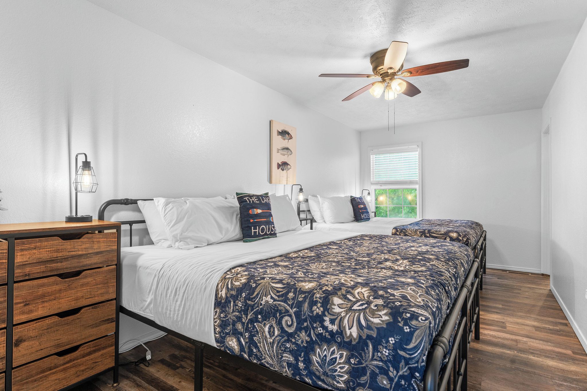 Une chambre à coucher comprenant un lit, un bureau, une chaise, un ventilateur de plafond et une fenêtre.