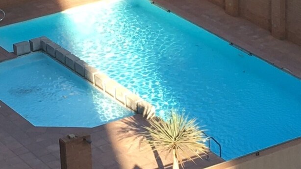 A rectangular swimming pool with a clear blue water surface, surrounded by a brick wall and a concrete deck.