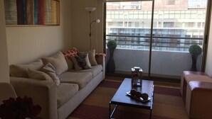 A living room with a sofa, a coffee table, and a large window with a view of buildings.