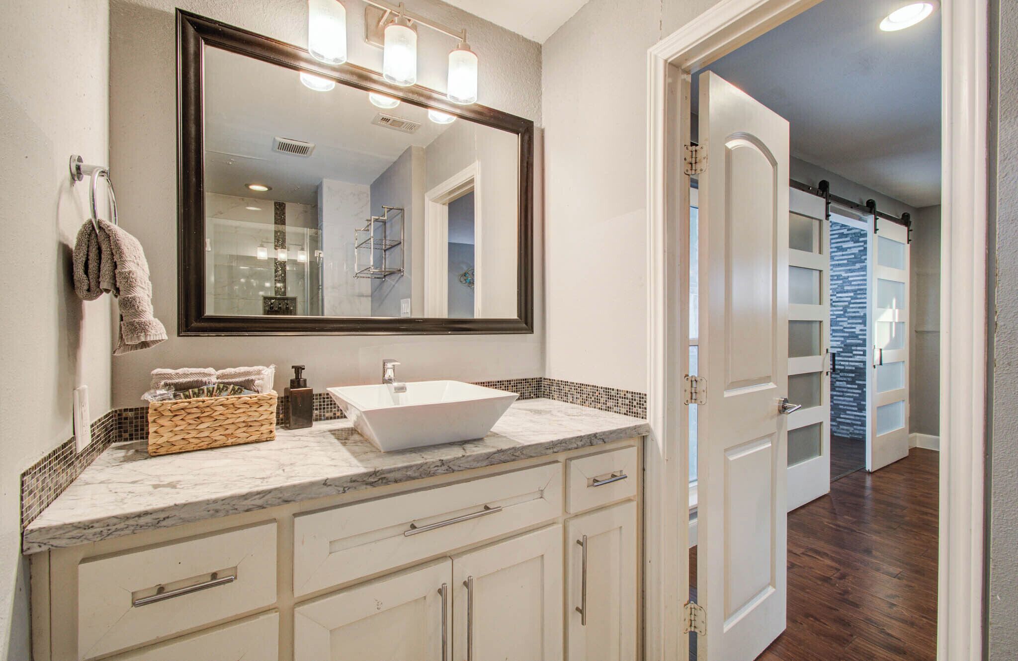 A bathroom with a large mirror, a white sink, and a marble countertop.