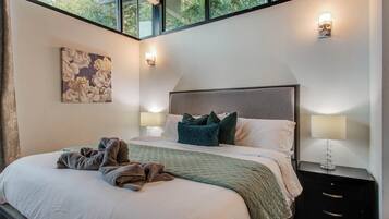 Un dormitorio con una cama grande, dos mesitas de noche con lámparas, un cuadro en la pared y una ventana con vistas a árboles.