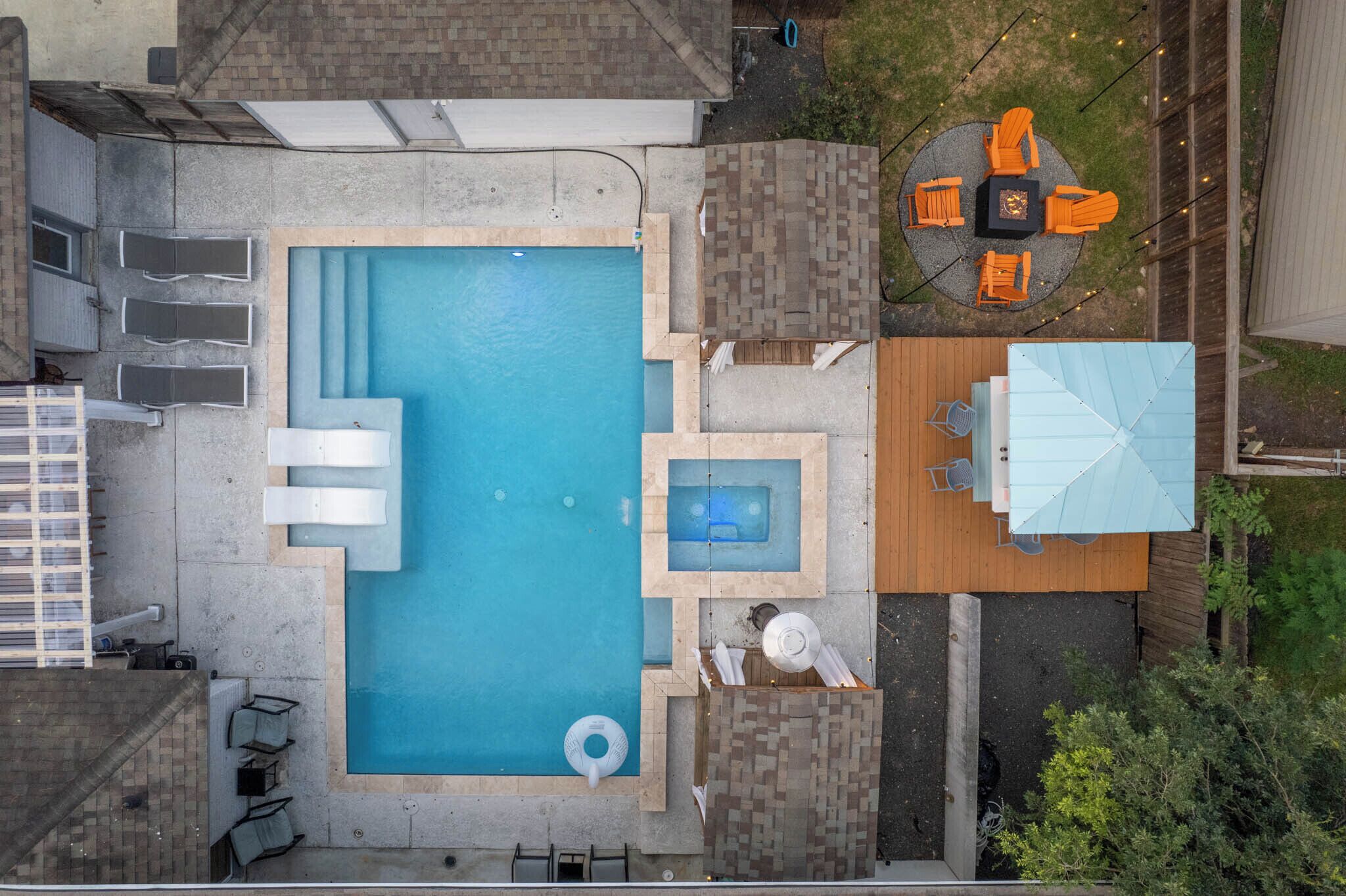 An aerial view of a backyard with a rectangular swimming pool, a hot tub, and a wooden deck with outdoor furniture.