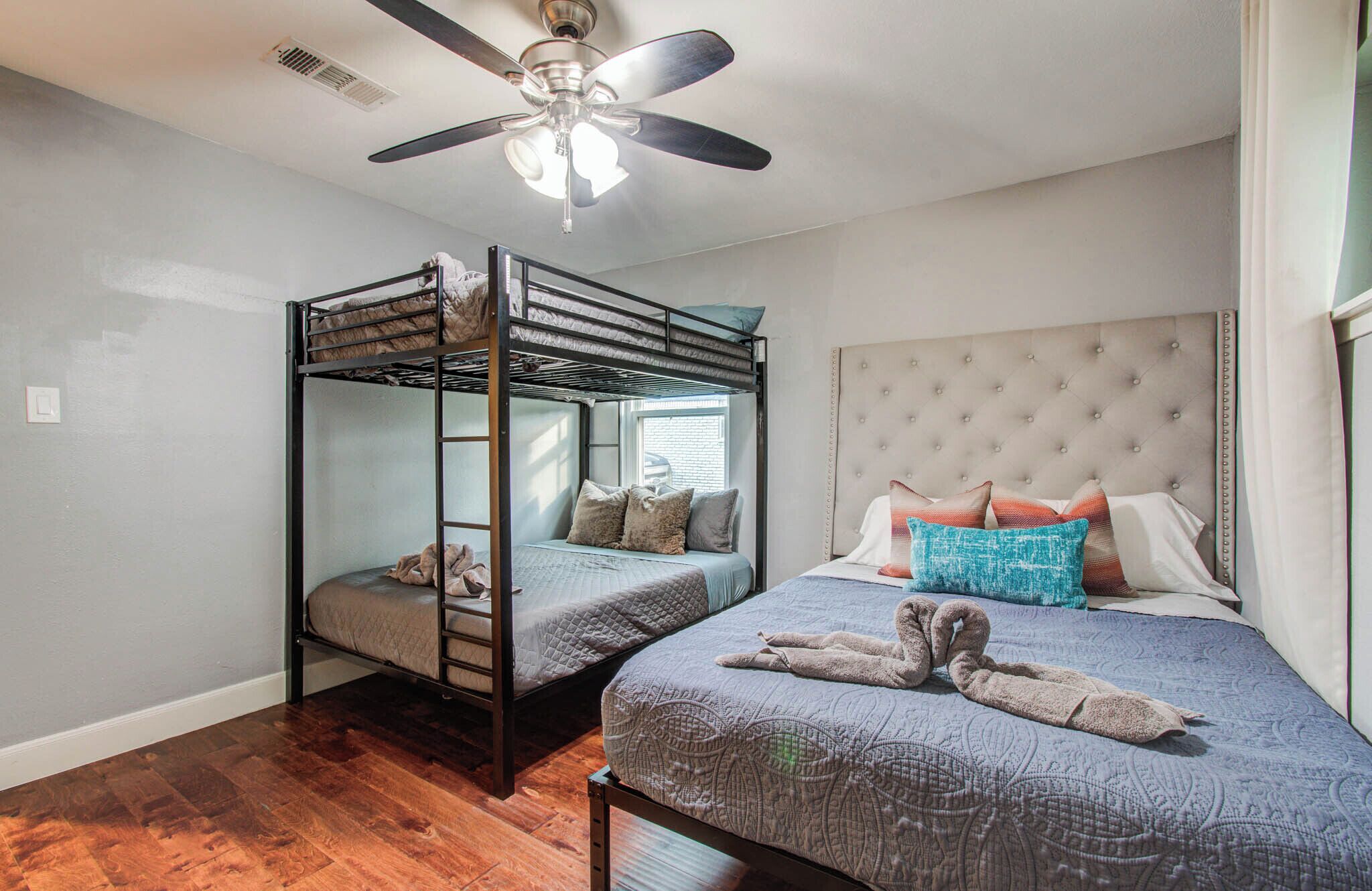 Una habitación con una cama doble, una cama individual con cabecera capitonada y un ventilador de techo.