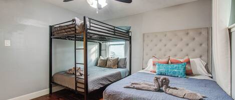 Una habitación con una cama doble, una cama individual con cabecera capitonada y un ventilador de techo.