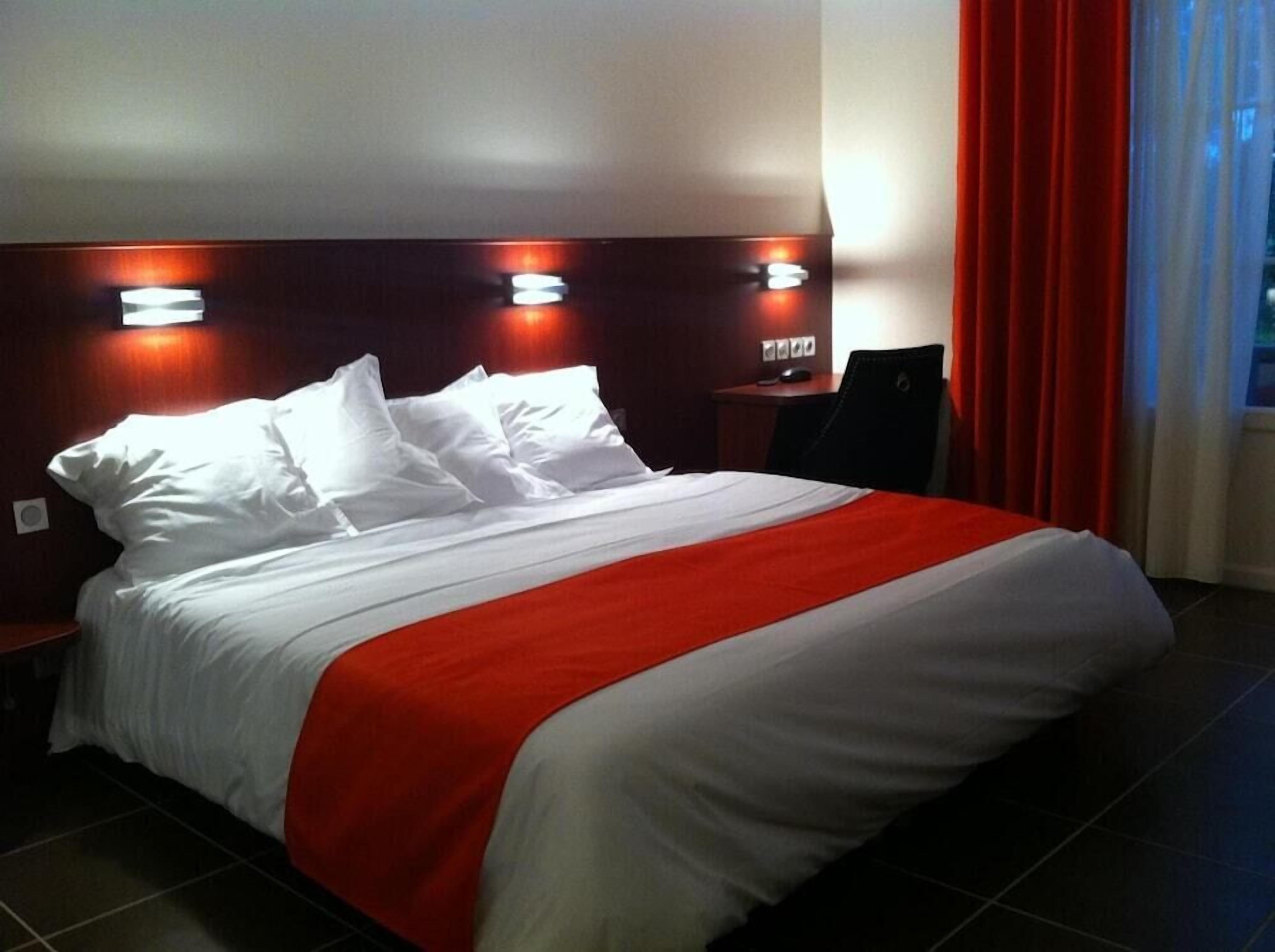 Une chambre d’hôtel avec un lit, des rideaux rouges et une table de chevet avec une lampe.