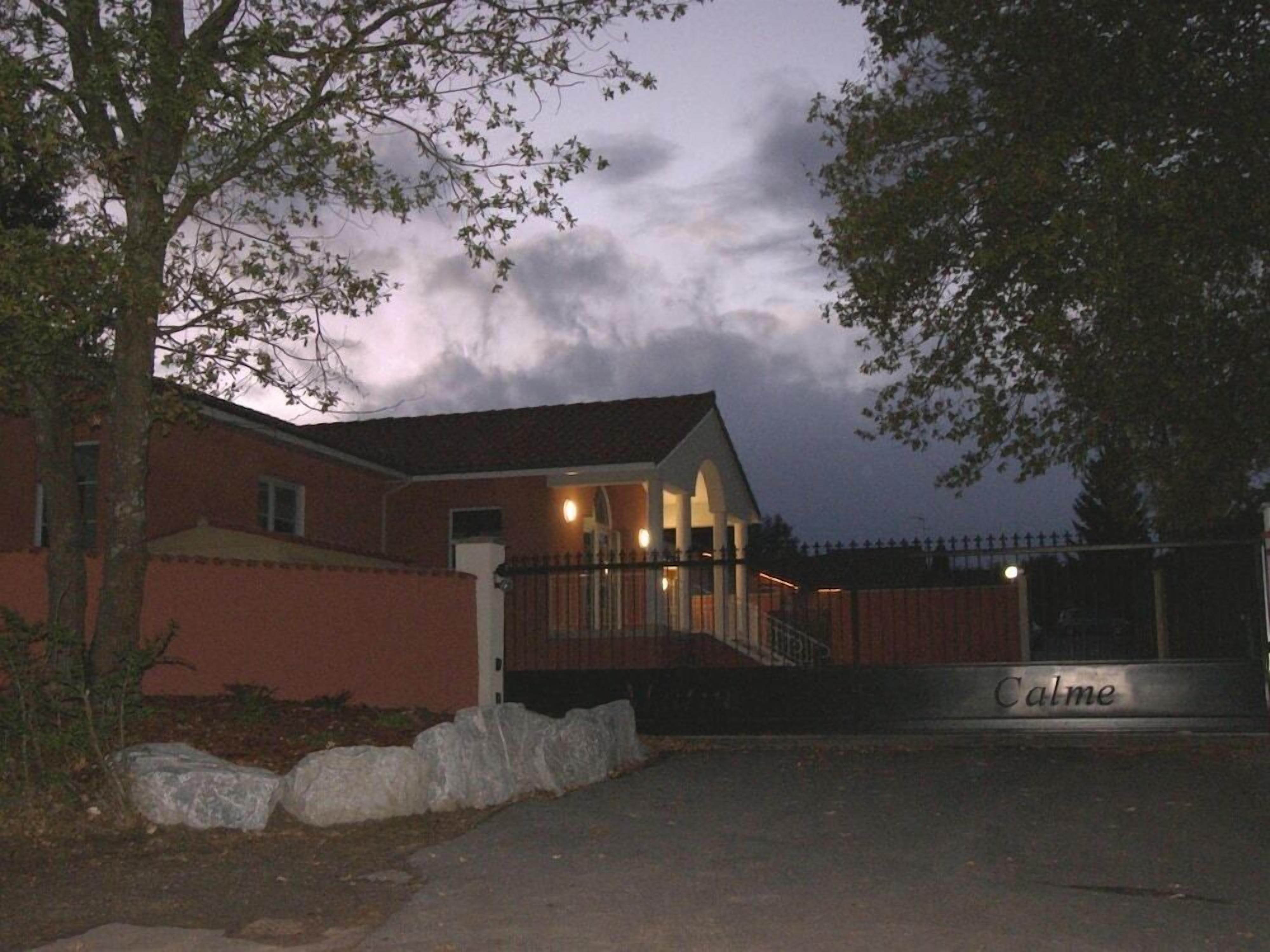 Een gebouw met een hekpoort, een overdekte veranda en een naambordje met de tekst 'Calme'.