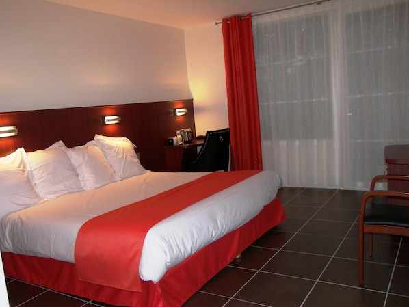 A hotel room with a large bed, a desk, a chair, and a window with curtains. - Hostellerie Du Matin Calme (Montverdun)