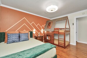 Quarto com cama beliche, cama com almofadas, mesa de cabeceira e parede com padrão geométrico.