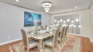 A dining area with a round table, chairs, a chandelier, a painting, and a patterned rug. - Empress Outdoor Luxury Villa (Houston)