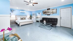 A bedroom with a bed, a ceiling fan, a coffee table, a black sofa, and a white door. - Empress Outdoor Luxury Villa (Houston)