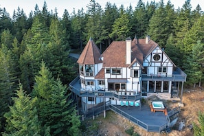 Uma casa grande e de vários andares com uma torre imponente, cercada por uma floresta densa.