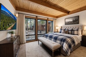 Ein Schlafzimmer mit einem großen Bett, einer Bank, einem Schminktisch, einem Fernseher und einem Gemälde.