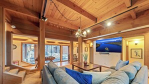 A spacious living area with a large sofa, wooden beams, a chandelier, and a large window offering a view. - Lx16 Luxe Martis Landing Sauna, Gameroom and Hot Tub (Truckee)