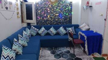 A blue sofa with zigzag pillows, a hexagonal patterned rug, and a decorative wall with a clock and string lights.