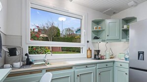 Cozinha com armários azul claro, bancada branca, geladeira de aço inoxidável e janela com vista para um jardim.