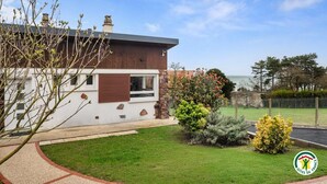 Uma casa moderna com fachada de pedra, janela com persianas e um jardim bem cuidado com arbustos e flores variadas.