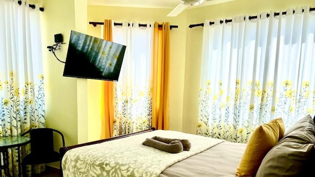 Hotellihuone, jossa on sänky, seinälle asennettu televisio, työpöytä ja kukkakuviolliset verhot.