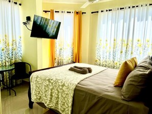 Habitación de hotel con cama, televisor montado en la pared, escritorio y cortinas con estampado floral.
