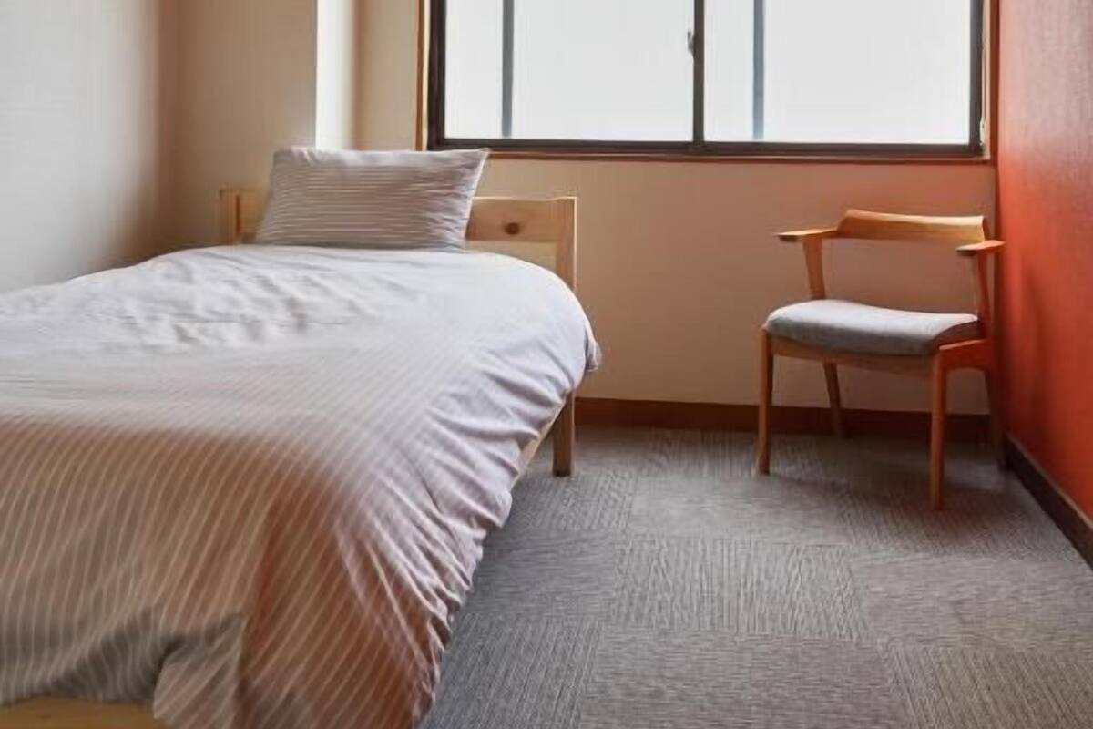 A bedroom with a bed, a chair, a window, and an air conditioning unit.