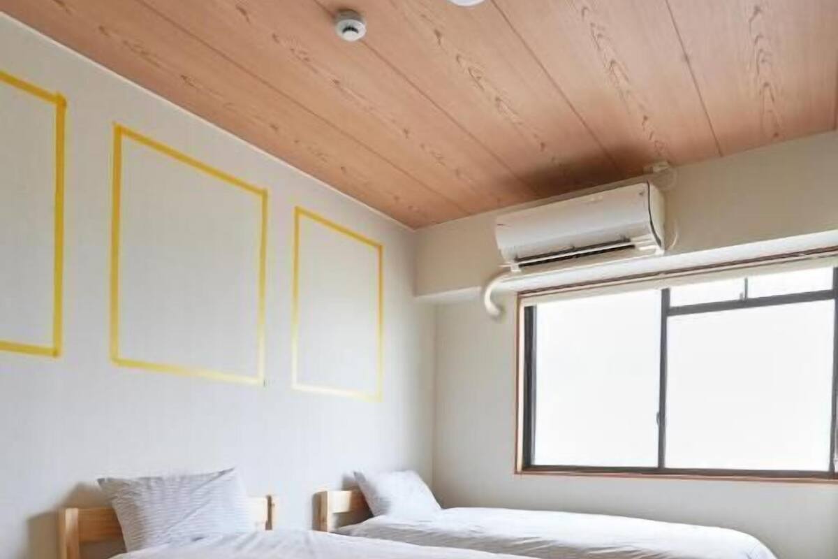 A bedroom with two beds, a window, and an air conditioning unit.