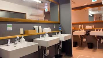 A modern bathroom with three sinks, a mirror, and a trash bin.