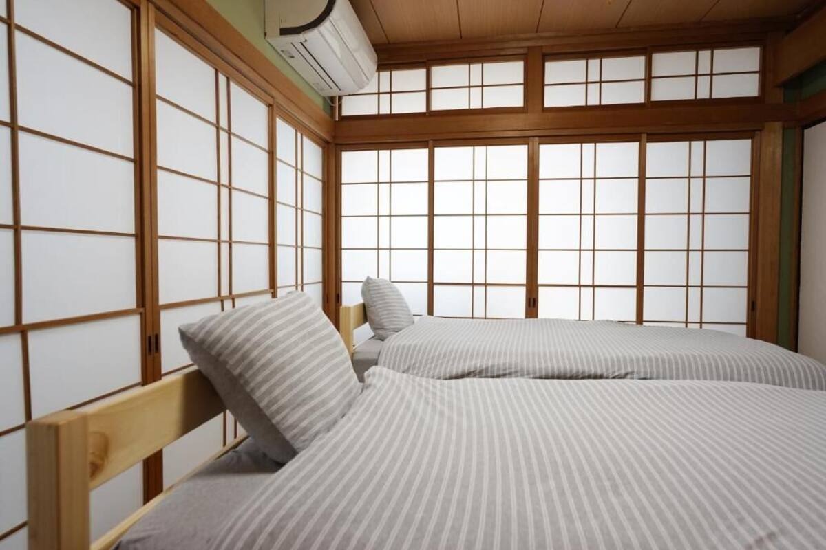 A room with a traditional Japanese-style sliding door, a bed with striped bedding, and an air conditioning unit mounted on the wall.
