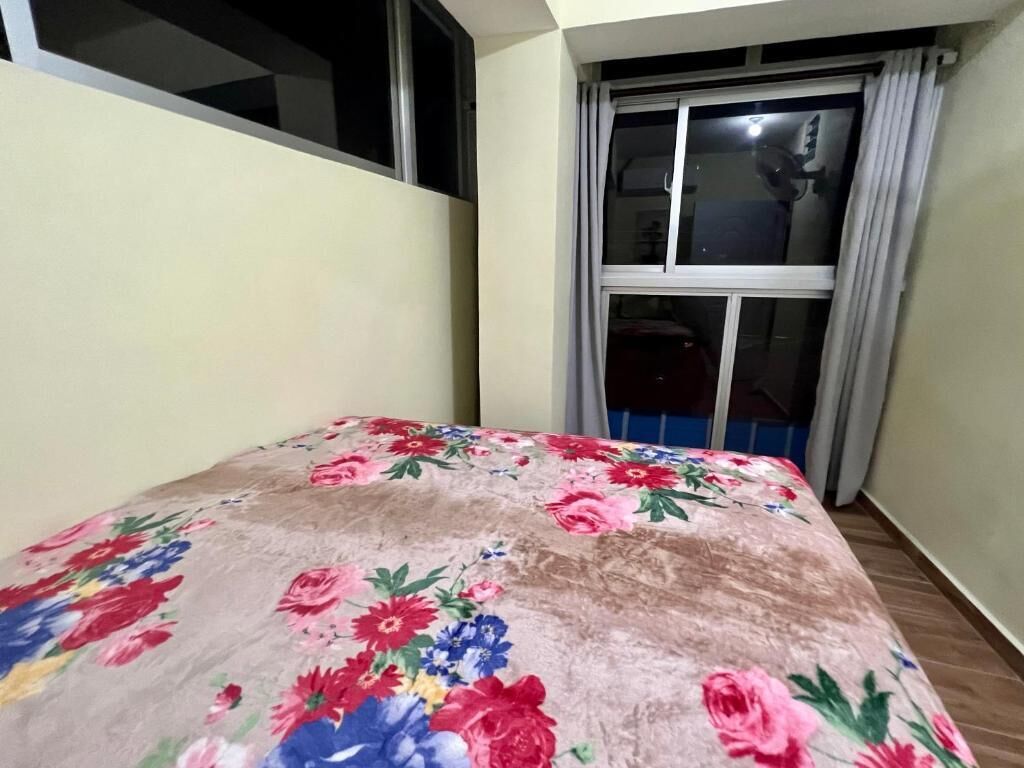 A bedroom with a floral bedspread, a window with curtains, and a view of the outside.