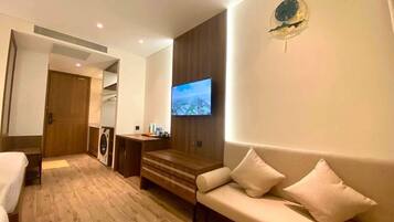 A hotel room with a wooden floor, a sofa, a television, a wooden cabinet, and a door leading to a bathroom.