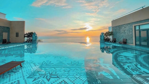 A infinity pool with a sunset view, surrounded by modern architecture. - APEC CHAMPA MUI NE BINH THUAN CONDOTEL (Tuy Hoa)