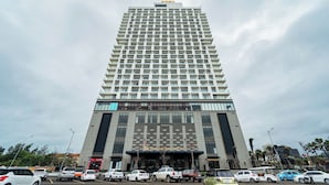 A tall hotel with a modern design, featuring a prominent APEC logo at the top. - APEC CHAMPA MUI NE BINH THUAN CONDOTEL (Tuy Hoa)